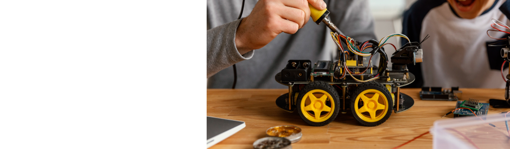 Personne soudant un robot à roues jaunes sur une table
